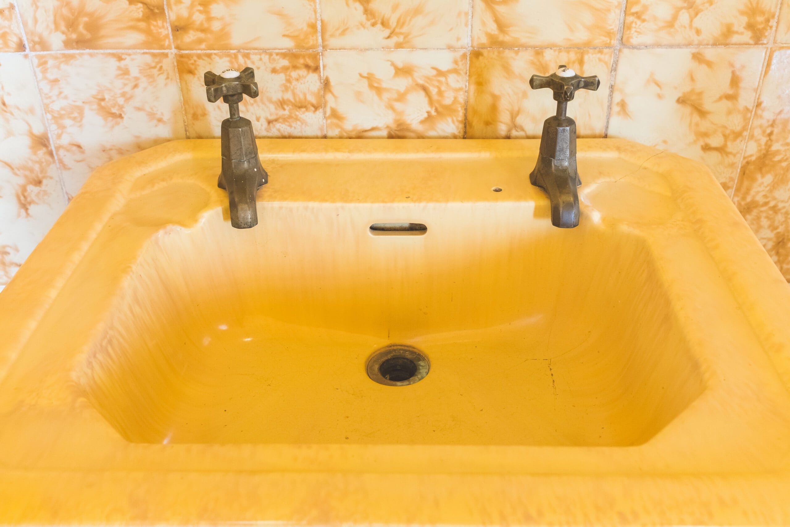 Vintage, yellow bathroom sink with old, outdated faucets