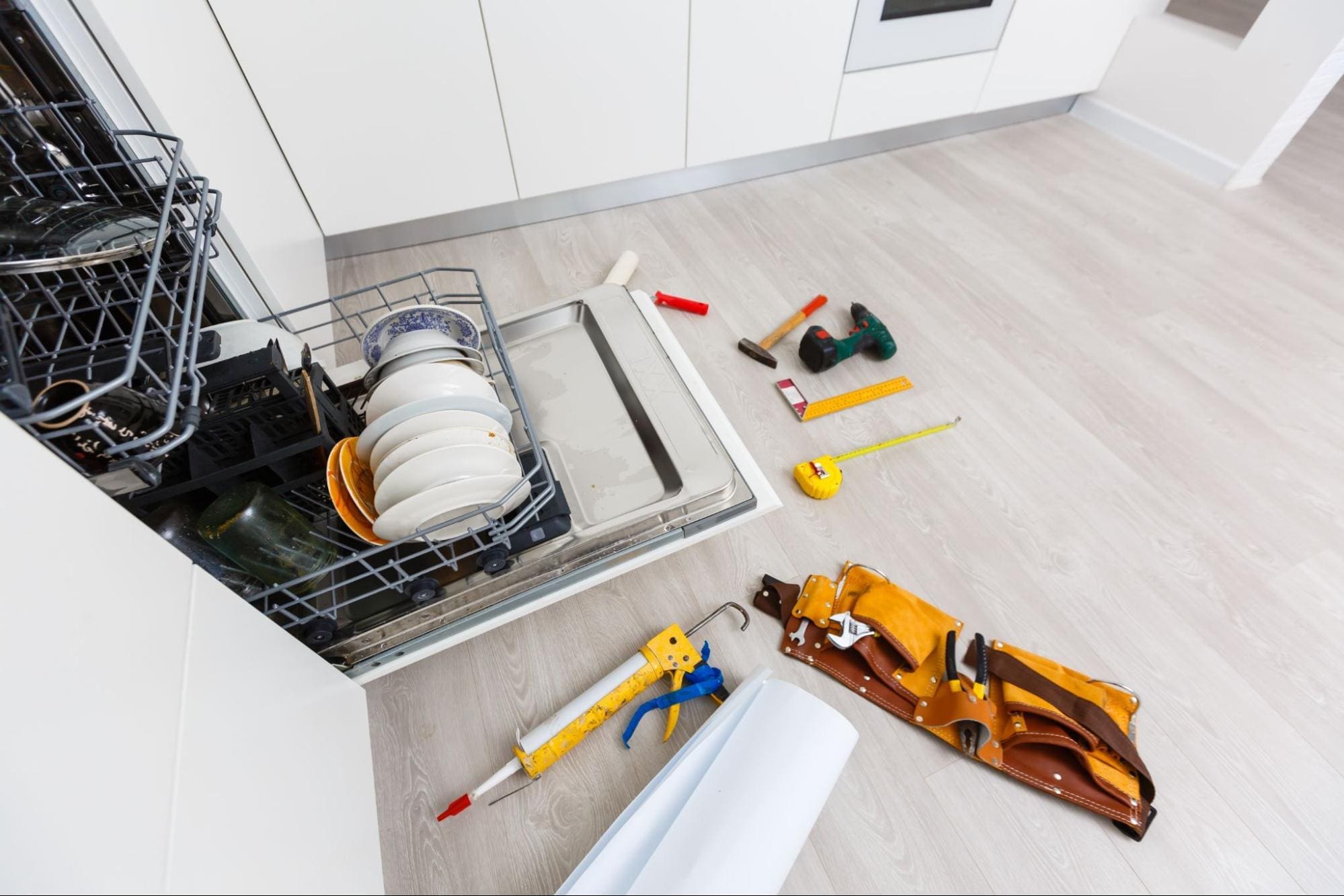 Newer dishwasher being repaired again due to the effects of hard water-dishwasher is open, tools out on the floor